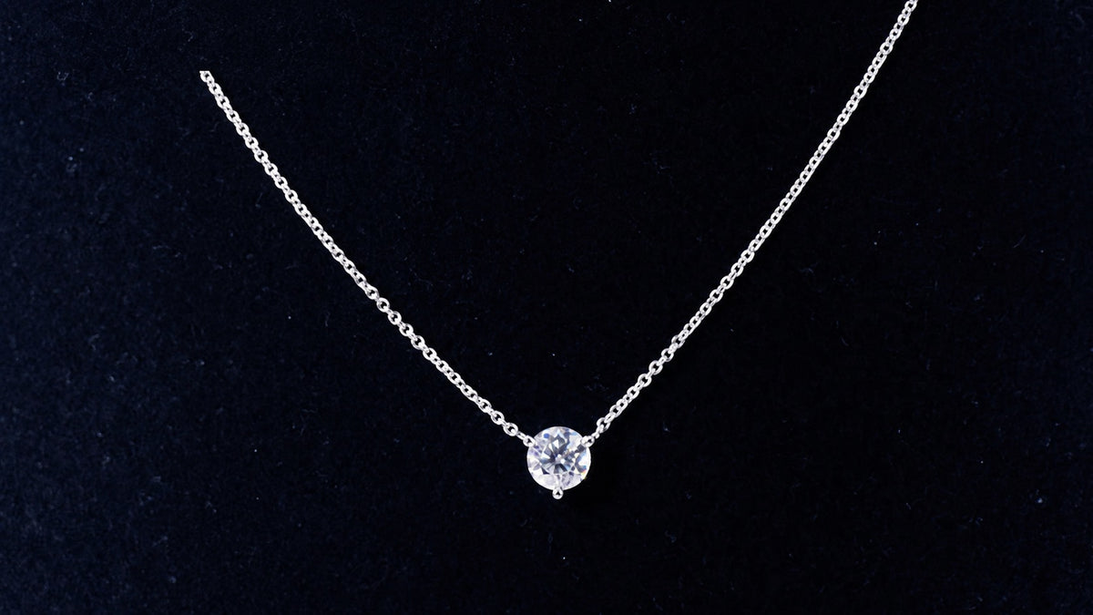 White gold solitaire moissanite necklace on a black display
