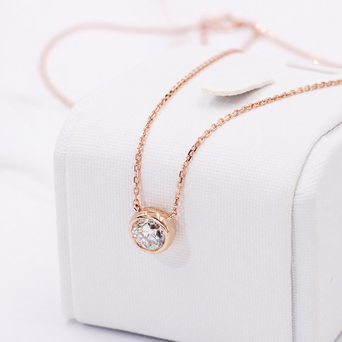 Rose gold bezel moissanite necklace draped over a white display