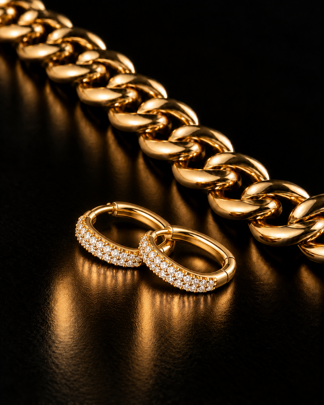 Editorial styling of stone-set gold hoop earrings beside a sculptural gold-coloured chain on glossy black.