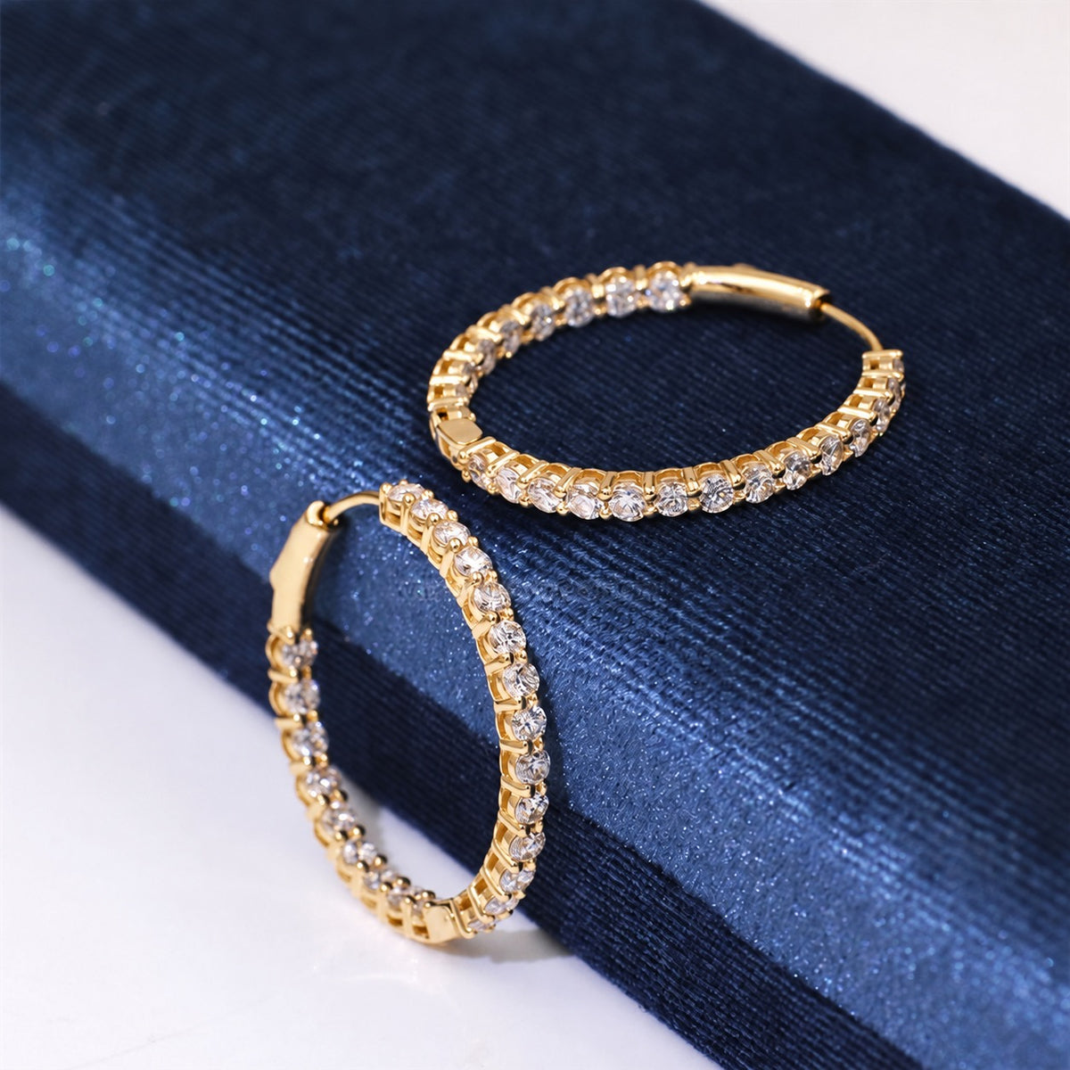 Yellow gold diamond hoops on dark fabric