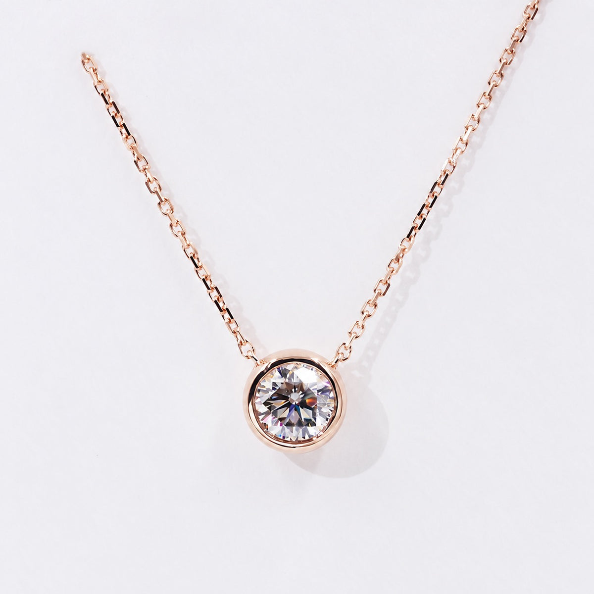 Round moissanite in a rose gold bezel on white